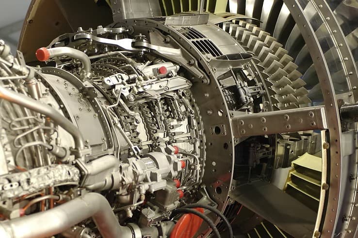 Intricate internal components of a jet engine showing complex piping, wiring, and metal turbine blades.