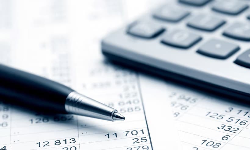 A black pen rests on financial spreadsheets with a calculator in the blurred blue background.