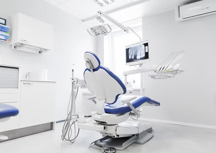 Modern dental clinic interior with a blue chair, overhead lamp, and digital X-ray display.