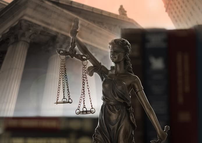 Lady Justice statue holding scales, superimposed over a blurred courthouse and law books background.