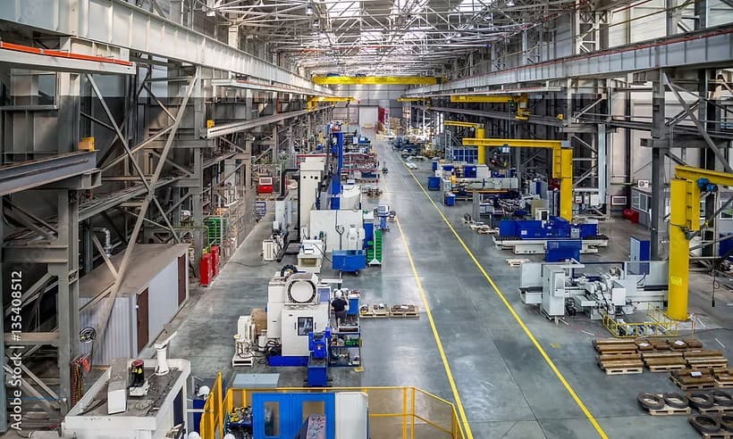Large industrial factory floor featuring heavy machinery, yellow overhead cranes, and steel structural beams.